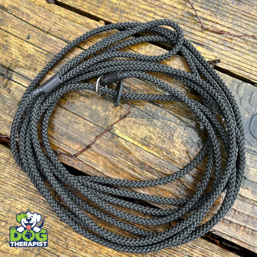 A coiled black braided dog leash with a black plastic buckle, placed on a rustic wooden plank surface. A &